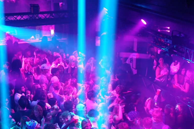 Cyan beams over a packed floor, seen from the balcony