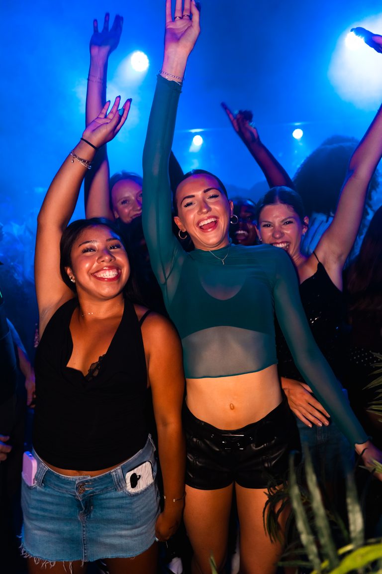 Friends mid-dance with arms up under blue light