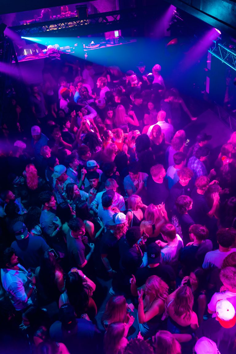 A wall-to-wall dance floor in magenta light, seen from the balcony