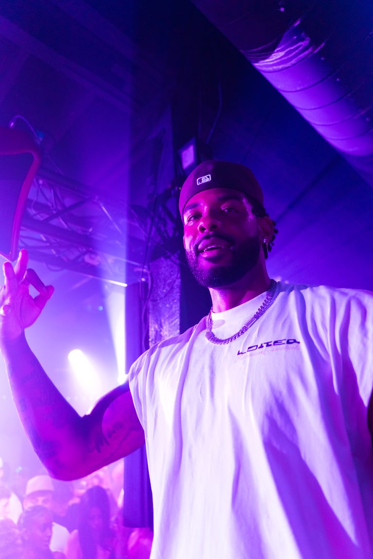 The DJ with a hand up in a purple wash