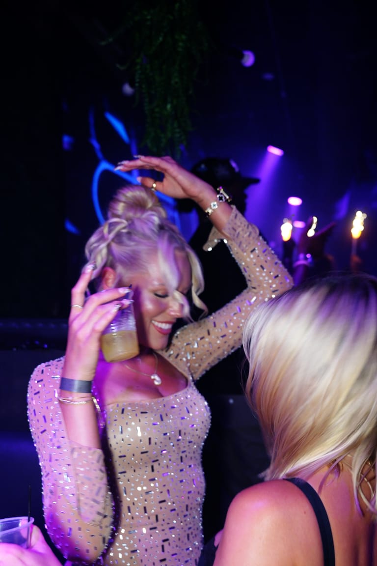 A guest dancing with an arm up under purple light