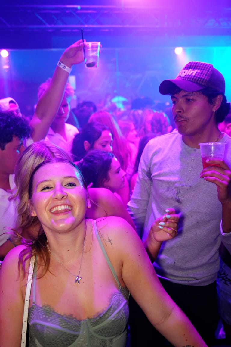A guest smiling on a packed floor under purple light