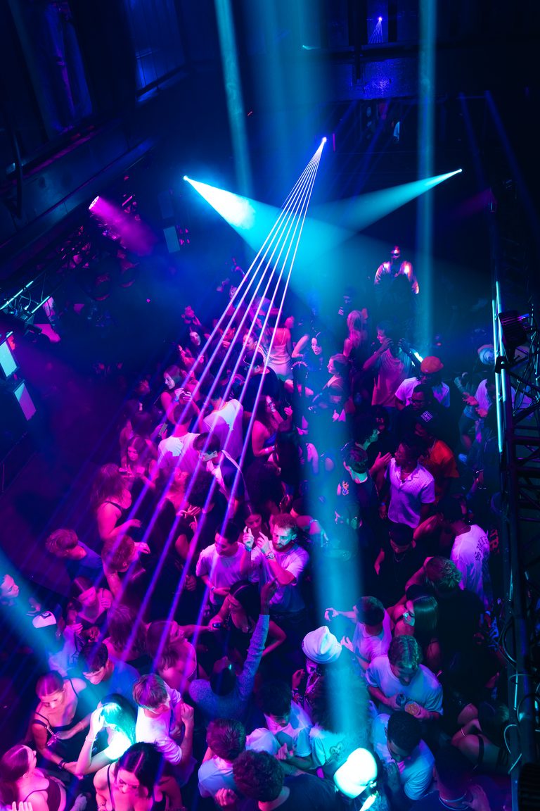 A cyan laser fan and pink wash over the crowd
