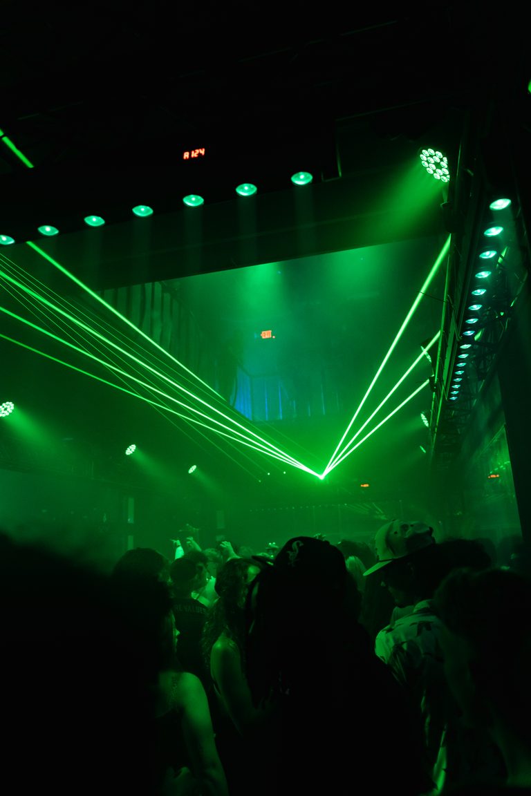 A green laser show over the stage with the crowd in silhouette